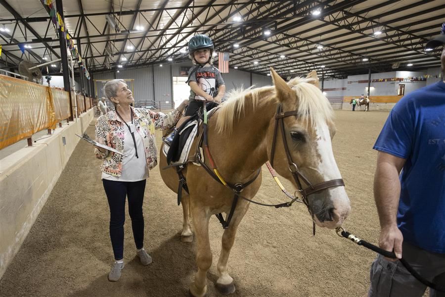 Isis walks beside a horse and looks up to a child.